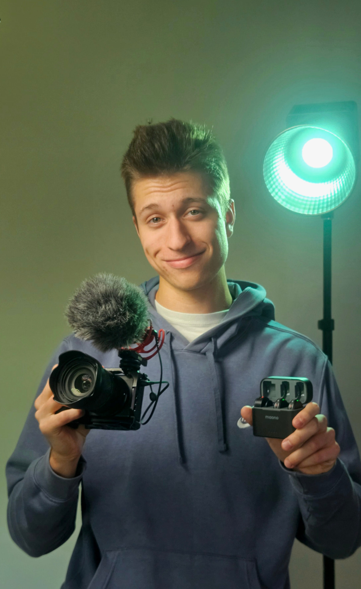 Mr White holding a camera and wireless microphone in front of a teal studio light